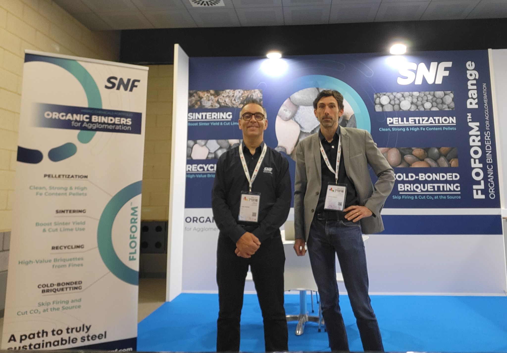 SNF exhibition booth showcasing organic binders for mining, with two representatives standing in front of product displays and banners.