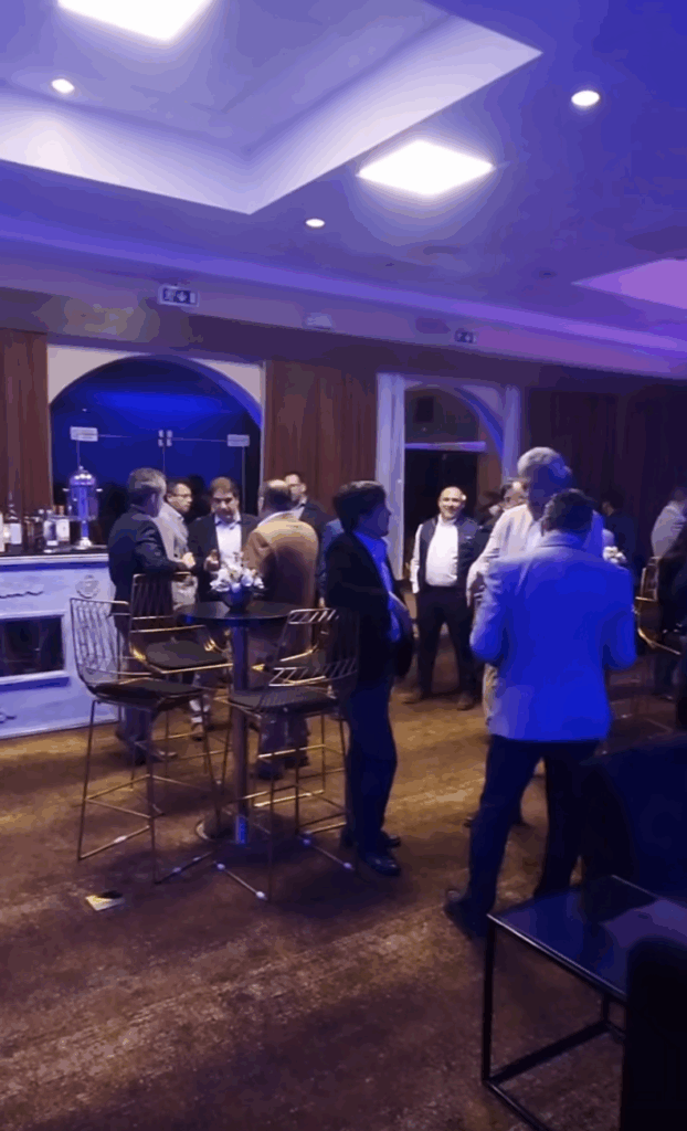 People networking during a professional indoor cocktail event, standing around high tables in a relaxed business atmosphere.