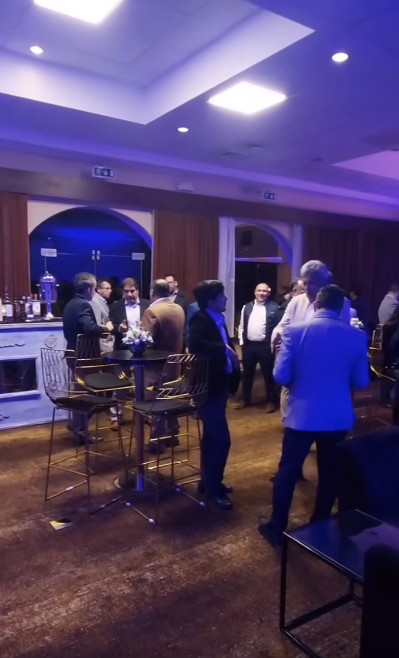 People networking during a professional indoor cocktail event, standing around high tables in a relaxed business atmosphere.