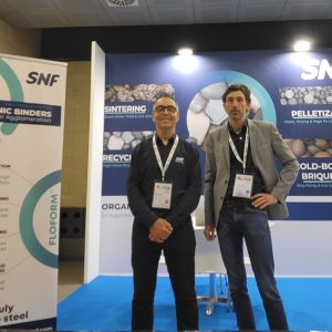 SNF exhibition booth showcasing organic binders for mining, with two representatives standing in front of product displays and banners.