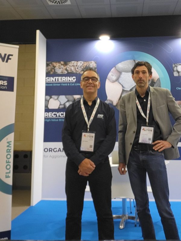 SNF exhibition booth showcasing organic binders for mining, with two representatives standing in front of product displays and banners.