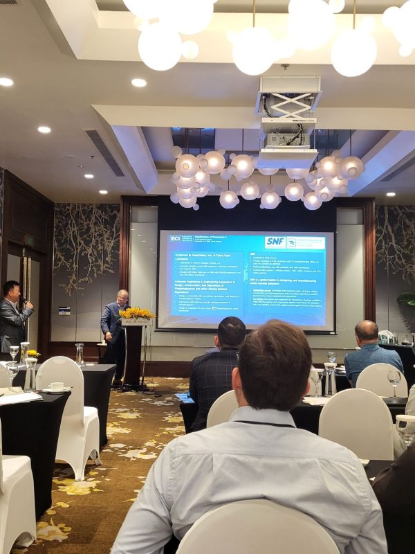 Conference room with attendees watching two speakers present slides about mining and phosphate innovation during an industry event.