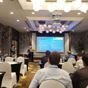 Conference room with attendees watching two speakers present slides about mining and phosphate innovation during an industry event.