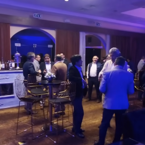 People networking during a professional indoor cocktail event, standing around high tables in a relaxed business atmosphere.