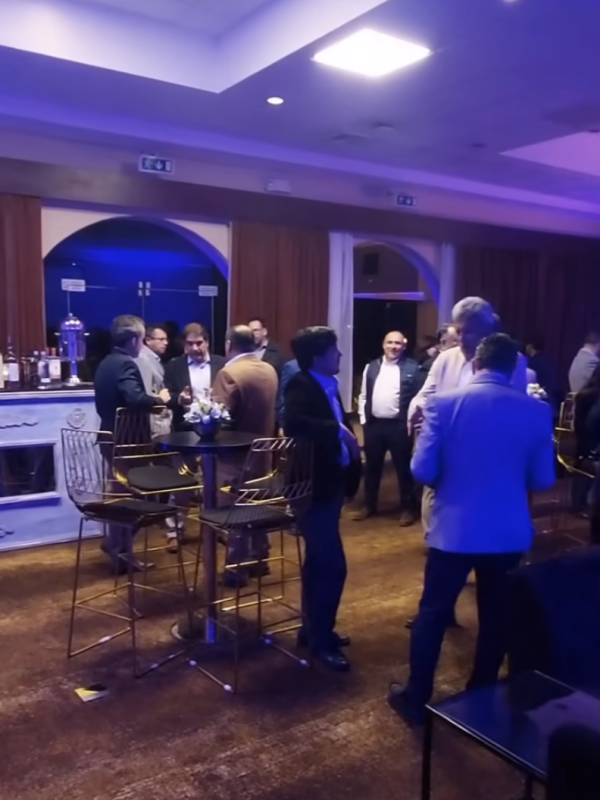 People networking during a professional indoor cocktail event, standing around high tables in a relaxed business atmosphere.