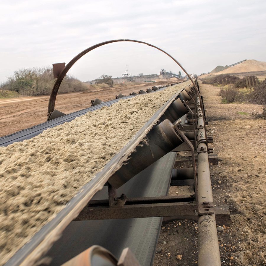 Mining conveyor transporting ore highlighting material flow challenges such as moisture variability, stickiness, and belt clogging.