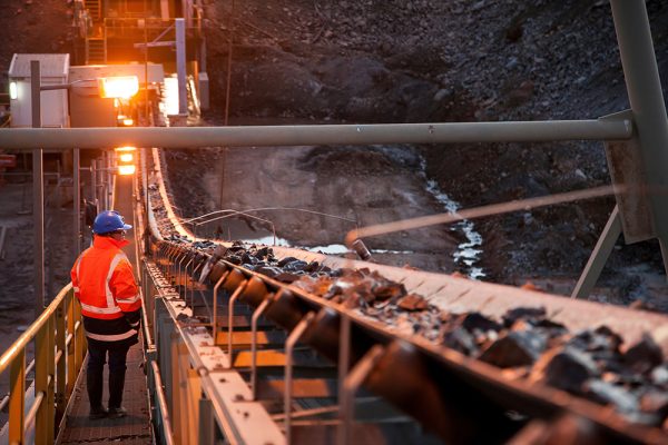 Mining operator monitoring conveyor system affected by moisture-related material buildup.