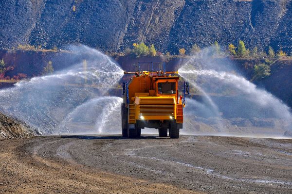 Mining water truck applying dust control treatment on haul road surface.